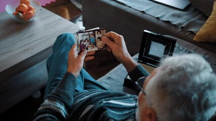 Grandpa sits on the couch at home and remembers fond memories of the past looking at old family pictures