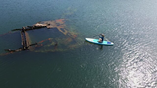 Aerial shot. Young women is having fun. Stand Up Paddling in the sea. SUP. Paddling among debrees of a sunk metal ships