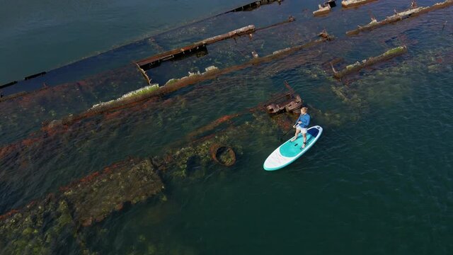 Aerial shot. Young women is having fun. Stand Up Paddling in the sea. SUP. Paddling among debrees of a sunk metal ships