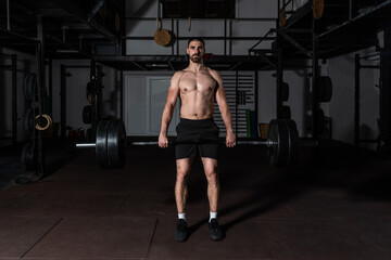 Fototapeta na wymiar Young sweaty strong muscular fit man with big muscles holding heavy barbell weight and starting hardcore weightlifting or deadlift workout cross training in the gym real people exercising