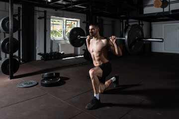 Young sweaty active muscular strong fit man with big muscles doing one leg squats in the gym with heavy barbell weights as hardcore strength workout cross training for strong legs and gluteus muscles