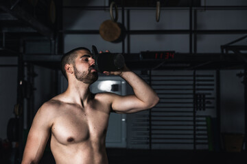 Fototapeta na wymiar Muscular man taking a break from a hardcore workout while drinking water. Young male with big muscles resting after weight cross training ion the gym. Close up