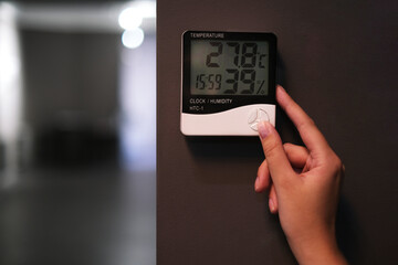 woman adjusts the psychrometer at home. device for measuring humidity and temperature on a dark wall close-up	