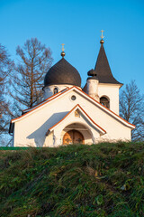 Fototapeta na wymiar A white stone orthodox church on a hill against clear blue sky and bare trees behind.