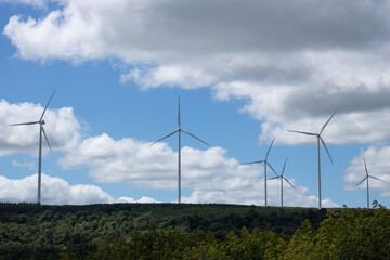 Wind Turbines farm in the hill a background of forest, blue sky and cloud.