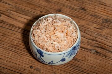 The dried small shrimps in the bowl or plate are on the wooden table