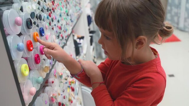 little girl chooses buttons, threads and accessories for patchwork in fabric store. Child dreams of sewing and picked up tailor. Cute little dressmaker working in atelier, handmade and handicraft
