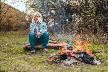 Traveler woman camping in the forest and relaxing near campfire after a very hard day. Concept of trekking, adventure and seasonal vacation.