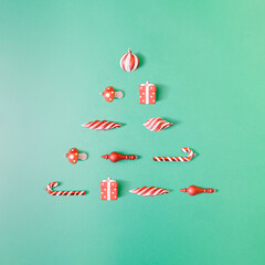 Minimal Christmas flat lay with colorful decorations on pastel green background. Creative xmas tree design.