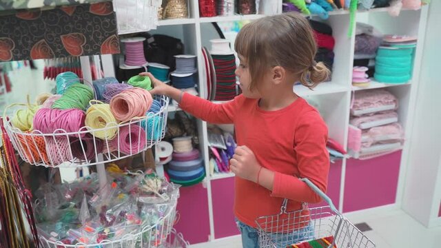 little girl chooses buttons, threads and accessories for patchwork in fabric store. Child dreams of sewing and picked up tailor. Cute little dressmaker working in atelier, handmade and handicraft