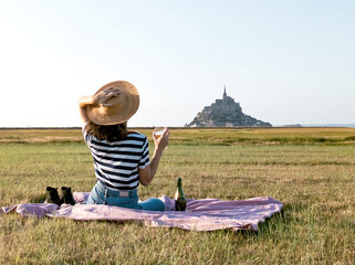 Young woman wearing hat picknick drink wine in front of mont saint michel 