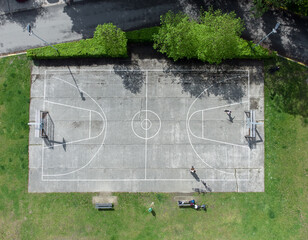 people at football and basketball court in a city park in Mortsel fort 4 near Antwerp in summer. Concrete sports ground by green grass. Drone aerial view from above