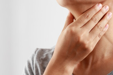 sore throat pain. Closeup of young woman sick holding her inflamed throat using hands to touch the ill neck in blue shirt on gray background. Medical and healthcare concept. Focus red on to show pain.
