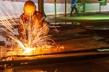 Male worker metal cutting spark on tank bottom steel plate with flash of cutting light close up wear protective gloves