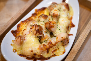 Baked cheesy sausage in white plate which is served in wooden tray. Appetize food object photo. Selective focus.