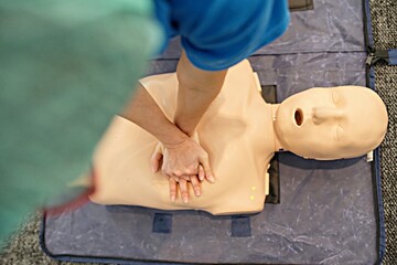 A top view of healthcare professional practices CPR chest compressions on a training dummy,...