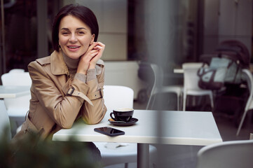 Toned photography, portrait of attractive cheerful young brunette woman in stylish casual wear smiling toothy smile looking at camera enjoying coffee break outdoors