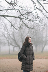 young woman walking in the foggy morning in autumn forest or park alone