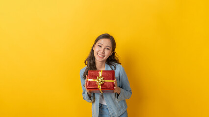 portrait pretty asian female in denim Jacket clothing smiling with red gift box board with copy space for text on yellow background, holiday festival, christmas celebration, happy hew year concept