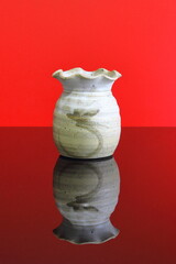 A ceramic vase on a dark reflective table with a red background.