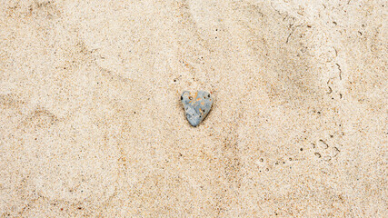 Heart-shaped gray sea rock on sandy beach