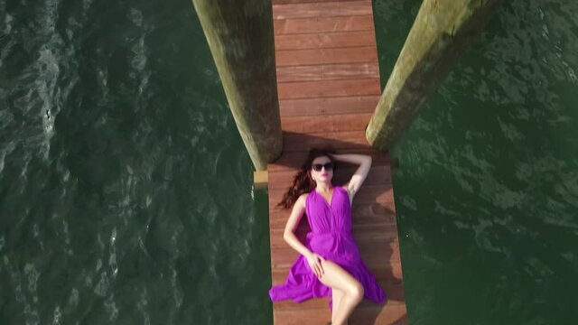 Attractive Female Model in Purple Dress Lying on Wooden Dock Above Sea, Top Down Aerial View