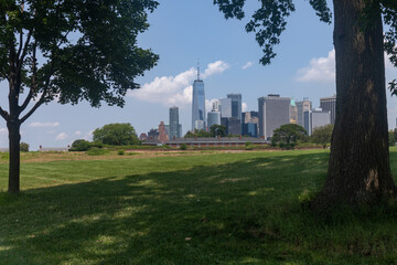 Lower Manhattan Skyline framed between Trees seen from a Green Grass Field on Governors Island in...