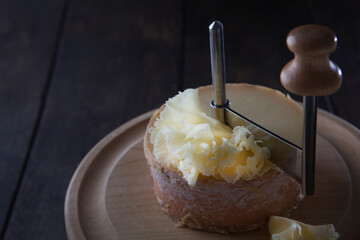 Thin shavings of tete de moine cheese. Special girolle knife. Cheese on wooden round board....