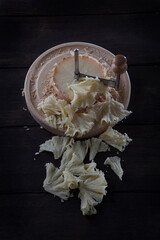 Swiss cheese tete de moine sliced into shavings on a round wooden surface. Scraper or girolle knife...