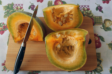 pieces of pumpkin with original yellow-green pulp on a wooden board are cut with a knife