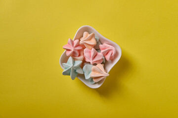 Multicolored meringue in a white saucer on a yellow background, close up
