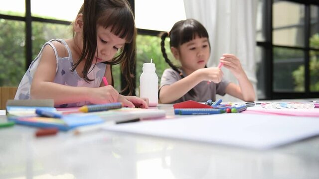 Two Asian girls practicing their artistic skills by drawing and painting, to Asian family and children concept.