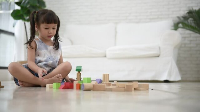 A 3 year old Asian girl is sitting, imagination and paying the wooden block toy, which is a toy that supports the development of children, to Asian girl and education concept.