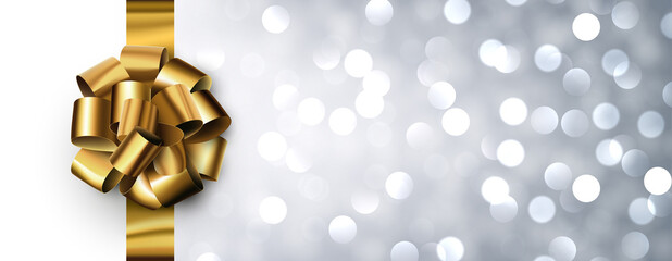 Golden foil ribbon with beautiful bow on silver bokeh background.