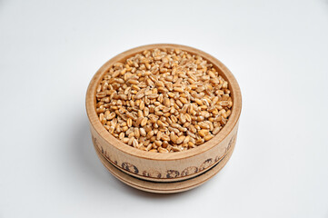 spelled grain in a wooden bowl on a white background