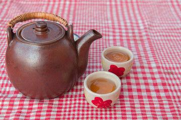 Top views reddish-brown ceramic teapot has two white ceramic tea cups placed on front. On table covered with red cloth , Concept tea for morning health, Natural tea set
