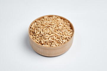 grains of oats in a wooden bowl on a white background