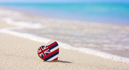 Flag of the Hawaiian Islands in the shape of a heart on a sandy beach. The concept of the best vacation in Hawaii