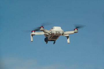 A drone flew from behind to the front against the blue sky background with an open plastic propeller.
