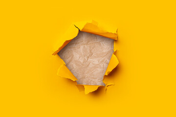 Bright yellow torn paper inside a hole wrinkled craft paper.