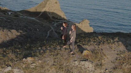 Two women in sportswear and barefoot doing yoga on the grass by the sea. Close-up aerial view - Powered by Adobe
