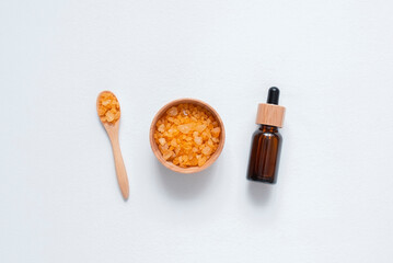 Wooden spoon, bowl filled with yellow bath sea salt and amber dropper bottle. Beauty treatment for spa and wellness. Skincare natural cosmetic concept for body care.