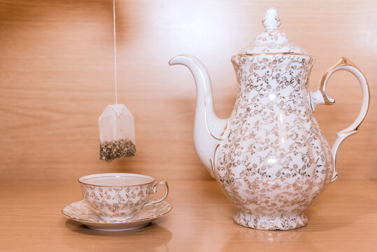 Juego de t&eacute; con adornos dorados. Sumergir una bolsita de t&eacute; en una peque&ntilde;a taza de t&eacute;. Fondo de madera