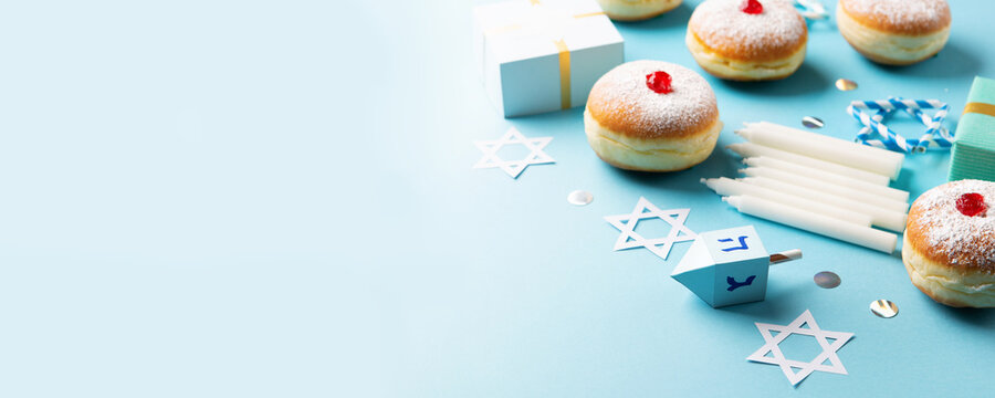 Jewish holiday Hanukkah concept - Hanukkah sweet doughnut with powdered sugar and fruit jam, gift boxes on blue paper background.
