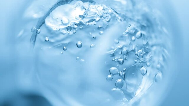 Top view macro shot of transparent liquid pouring into beaker creates a lot of bursting bubbles on blue background | Abstract face care cosmetics formulation concept