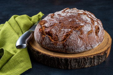 Freshly baked traditional country style wheat rye wholemeal bread. Single object on a wooden background with a green napkin. Front view