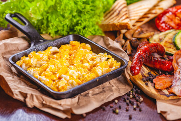 English breakfast with scrambled eggs, sausages, bacon, vegetables and spices
