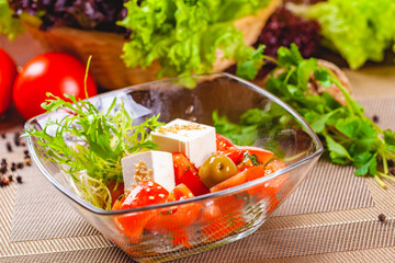 Salad with tomatoes, herbs and cheese in glass bowl