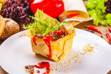 Salad with beef and chili pepper in flat bread basket on white plate