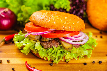 Hamburger with beef cutlet, tomatoes and onion rings on wooden cutting board